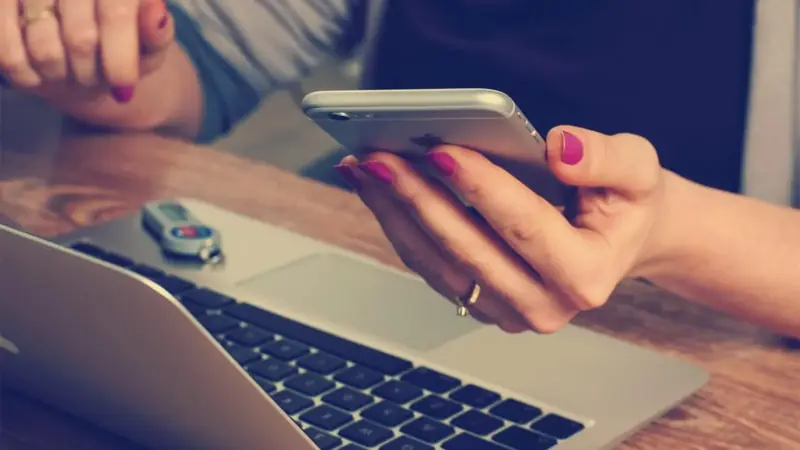 Hands holding a phone over a laptop